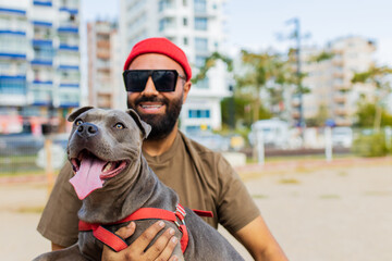 portrait of happy man in red hat and sunglasses with american terrier in dogs walking area park in sity