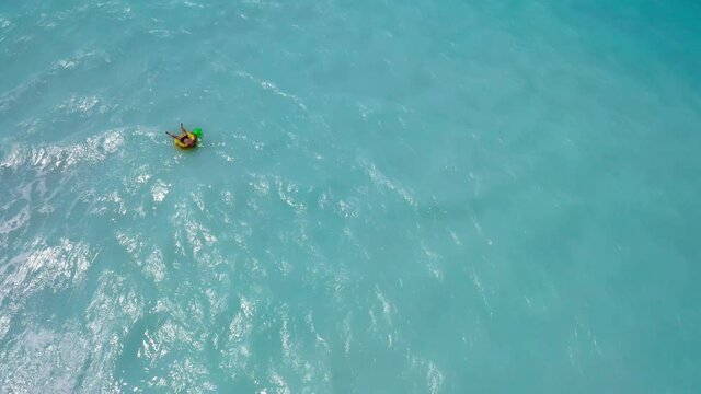 4K drone footage man floating on inflatable yellow ring on ocean waves in tropical weather. Recreation, relaxation, luxury summer holiday resort concept.