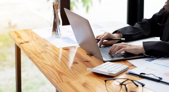 Close up Business woman using calculator and laptop for do math finance on wooden desk in office and business working background, tax, accounting, statistics and analytic research concept
