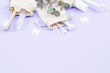 A set of toothbrushes, toothpicks, dental floss and toothpaste in cotton bags on soft lilac.