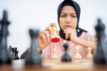 Muslim woman with hand holding chess pieces while playing chess