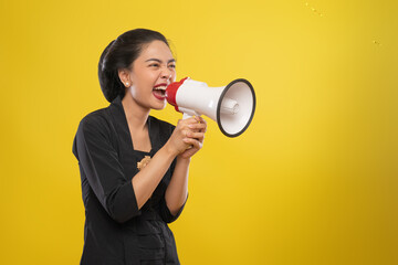 Asian woman wearing Kebaya shouts while holding megaphone on isolated background