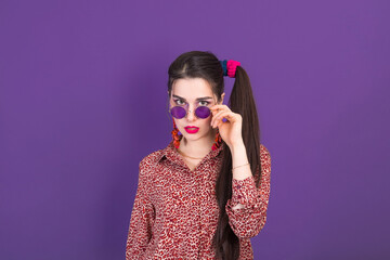 Portrait of cute young brunette dressed in 90s style on purple studio background.
