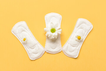 Menstrual pads and chamomile flowers on yellow background