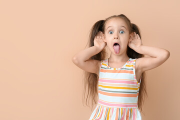 Portrait of little girl showing tongue on beige background