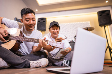 young asian boy playing guitar and his friend watching a music video