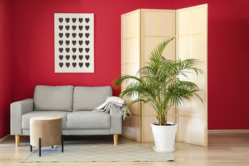 Stylish interior with sofa and folding screen near red wall
