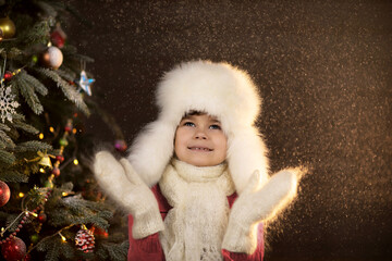 A boy in a fur hat and mittens rejoices in the Christmas snow