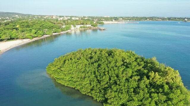 Aerial flyover green growing island surrounded by Caribbean Sea during summer - Santa Cruz de Barahona,Dominican Republic
