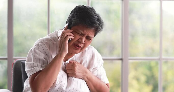60s Asian woman suddenly feels pain from heart attack using phone call to emergency medical center asking for ambulance. Concept of good conscious mind and self-care of lonely living senior people.