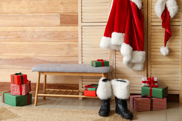 Obraz premium Santa Claus boots, costume and bench with gift boxes near wooden wall