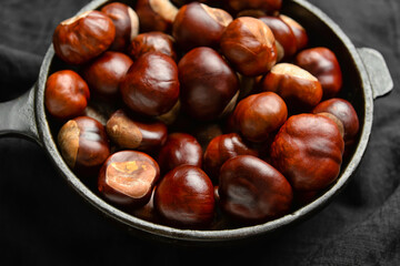 Frying pan with chestnuts on dark fabric background