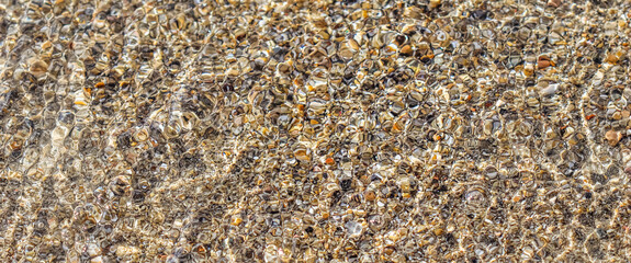 A background of sand, small pebbles and flowing waves on the sea beach. Summer vacation and coastal...