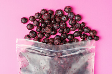 Packages with frozen blueberry on pink background, top view.
