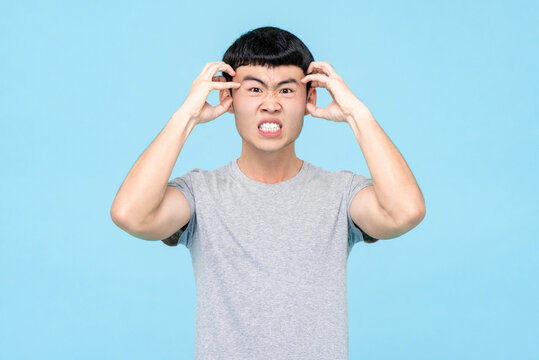 Young Asian man expressing angry emotion on isolated light blue studio background