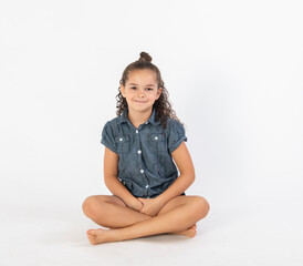 Mixed race little girl in denim romper sitting cross legged isolated on white background