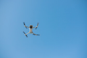 An electric drone is flying in the blue sky. 3D illustration. Drone: 3D model. Background: photopanorama.