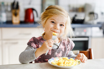 Lovely toddler girl eating healthy fried potatoes for lunch. Cute happy baby child in colorful...