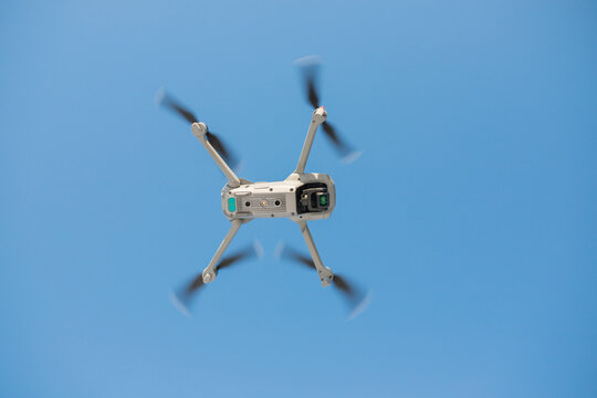 An electric drone is flying in the blue sky. 3D illustration. Drone: 3D model. Background: photopanorama.