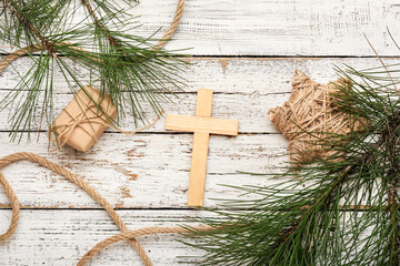 Cross with pine tree branches and gift on white wooden background. Concept of Christmas story