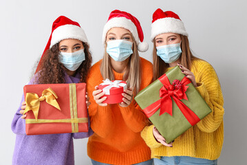 Beautiful young women in medical masks and with Christmas gifts on light background