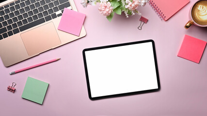 Top view female workspace with digital tablet, laptop and colorful sticky notes on pink background.