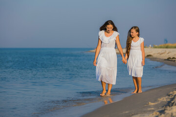 Fototapeta na wymiar mom and daughter in white dresses walk on the beach