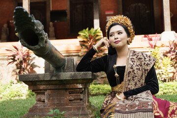 woman wearing Balinese kebaya sitting next to the statue