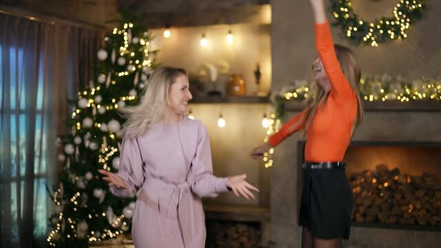 two blondes in festive clothes are laughing and jumping merrily against the background of a room decorated for Christmas