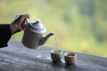Hand holding a hot tea mug pouring hot tea into the glass and nature background.