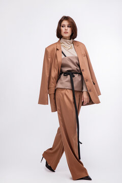 Fashion photo of a beautiful elegant young woman in a pretty oversize brown and beige suit, corset, jacket, pants posing over white background. Bob haircut. Studio Shot. Portrait