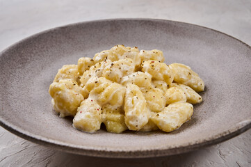 Close up homemade gnocchi, prepared with potato and whole grain flour dough with cream sauce and pepper on gray plate, selective focus