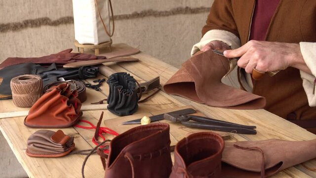Medieval Craftsmen Guilds. Master Craftsman. Historical European Leather workshop. Medieval schoenmaker leatherworker craftsmen. Craftsman sews by hand a wallet, shoes, belt, gloves