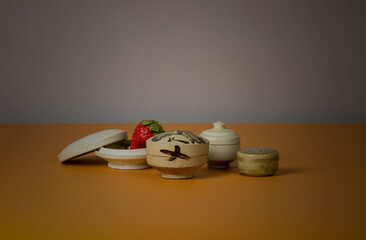 Still life of Chinese antique ceramics boxes with single strawberry against brown and gray background