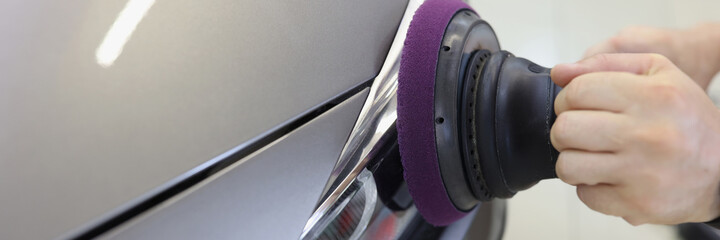 Hands with orbital polisher in car workshop polishing headlight of car