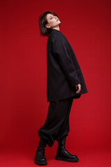 Fashion photo of a beautiful elegant young woman in a pretty oversize black suit, pants, top posing over red background. Bob haircut. Studio Shot. Rebellious free street style. Rebel and classic