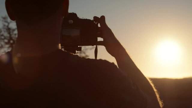 Dramatic handheld shot of a tourist photographer setting his camera on a tripod and proceeds to take a landscape photo with the sun flaring in a desert in Africa.