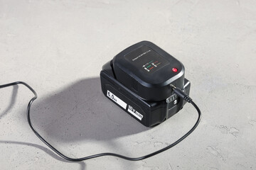 Powerful battery for electrical tool with connected charger on concrete gray surface close-up