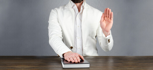 A man in a jacket holds his hand on a Bible. Pronouncing an oath with a raised hand. Oath on the...