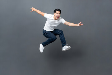 Young handsome energetic Asian man jumping with hands outstratched in isolated studio gray background