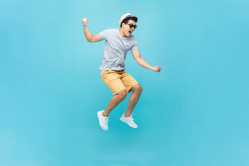 Young Asian tourist man jumping and yelling in light blue color studio isolated background - obrazy, fototapety, plakaty
