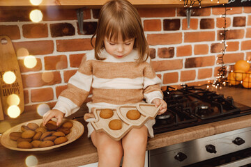 little girl holding a plate in the shape of a herringbone. there are cookies on the plate.
