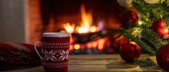 Hot chocolate cup, burning fireplace background. Christmas tree decoration, relaxation by the fire