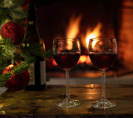 Red wine glasses, burning fireplace background. Christmas tree decoration