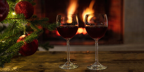 Red wine glasses, burning fireplace background. Christmas tree decoration