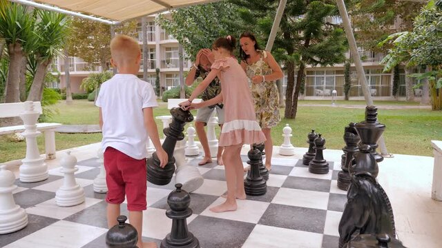 Emotional family having fun playing chess in the summer park. A fun open-air chess game with giant pieces.