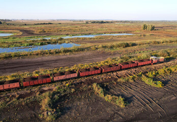 Train transports peat in freight wagons from peat extraction. Aerial view of the diesel locomotive on railroad in landscape at wetlands. Drone view of the peat bog railway at peatlands.