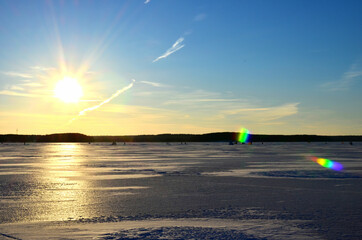 Two fishermen on a frozen lake catch fish in a hole of ice on the background of evening sunset....