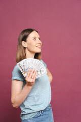 Funny young lady in a blue summer tshirt is holding money and looking to them over a pink background with copy space