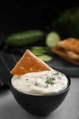 Tasty creamy dill sauce with cracker in bowl on grey table
